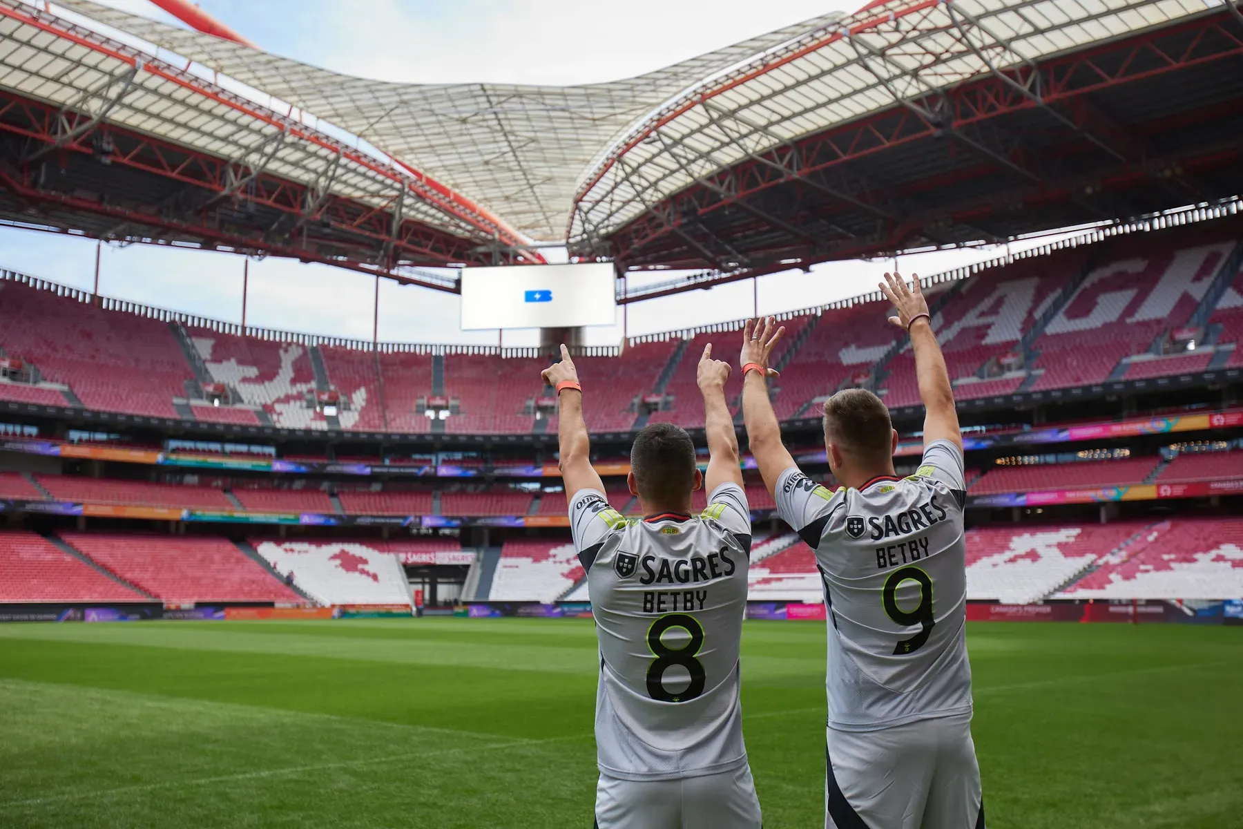 Betby players facing the empty stands of Estádio da Luz with the Betby logo on the screen